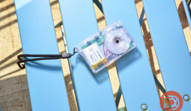 A small, transparent film camera with a wrist strap resting on a bright blue slatted bench.