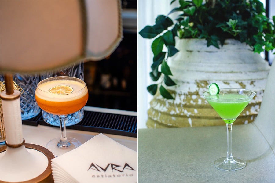 Two cocktails are shown side by side. The left cocktail is an orange drink in a coupe glass, garnished with a dried lemon slice, placed on a bar counter next to a lamp and napkins with 
