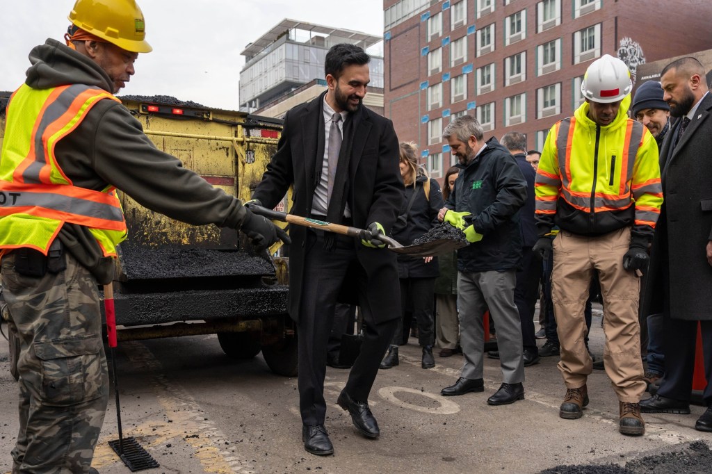 Mayor Mamdani holds a shovel with asphalt.