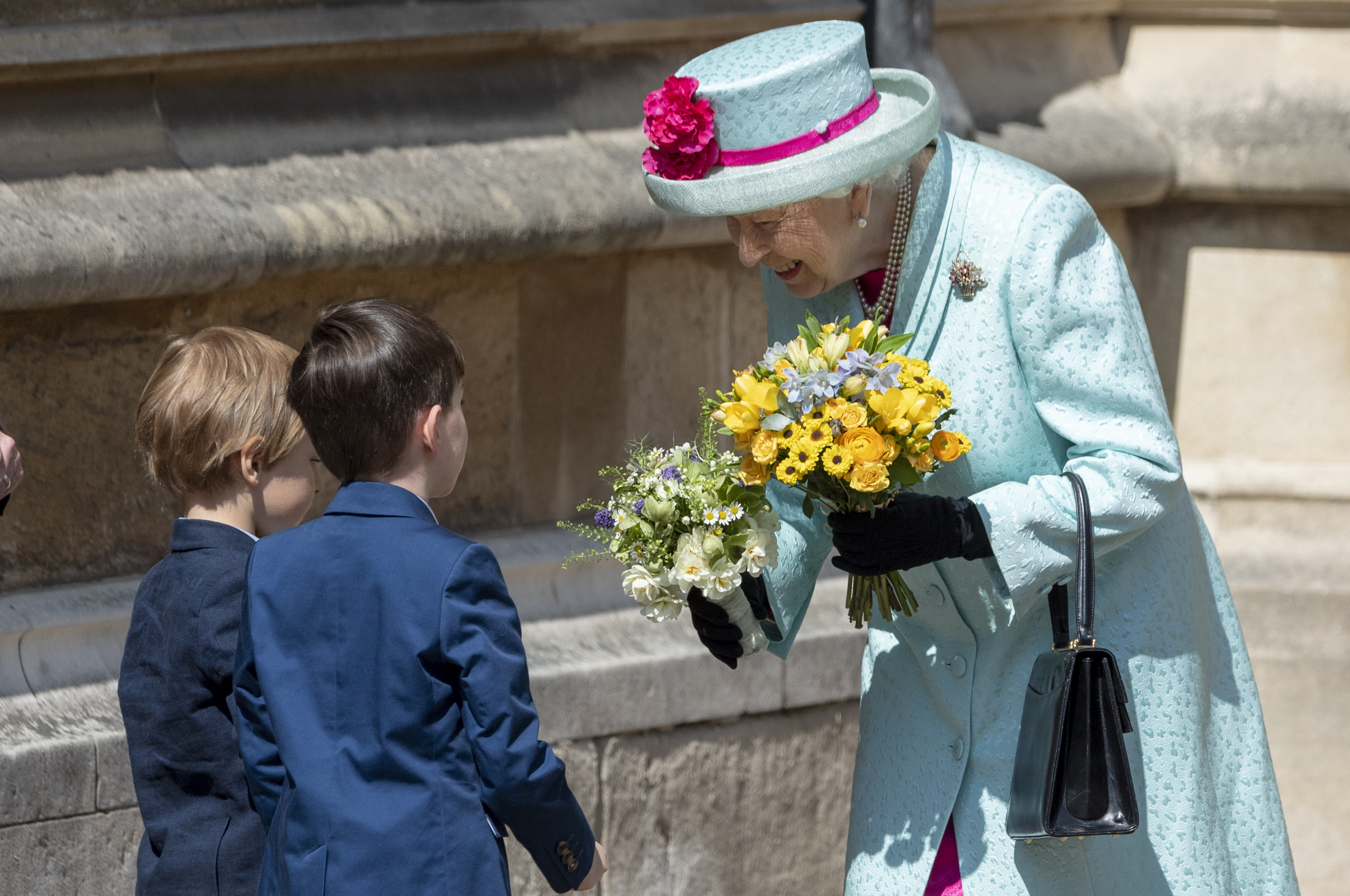 Queen Elizabeth in a turquoise coat taking flowers from two little boys