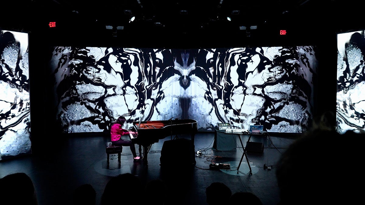 Clara Yang plays piano on a stage in front of abstract black and white graphics