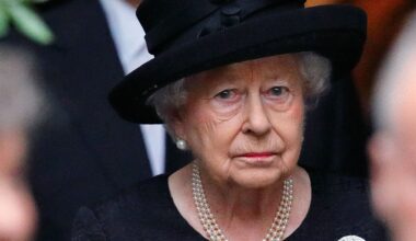 Queen Elizabeth II wears a black dress and matching hat and looks very sad while wearing a string of pearls