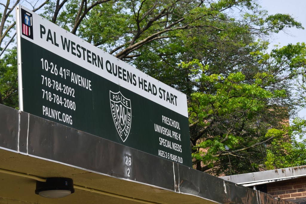 A large banner reading PAL western Queens head start in forest green. There are large tree branches behind the poster.