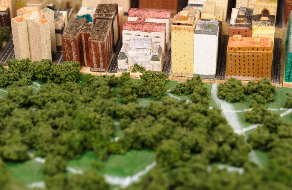 Close-up of model city blocks with varied buildings and a green park area with trees and pathways.