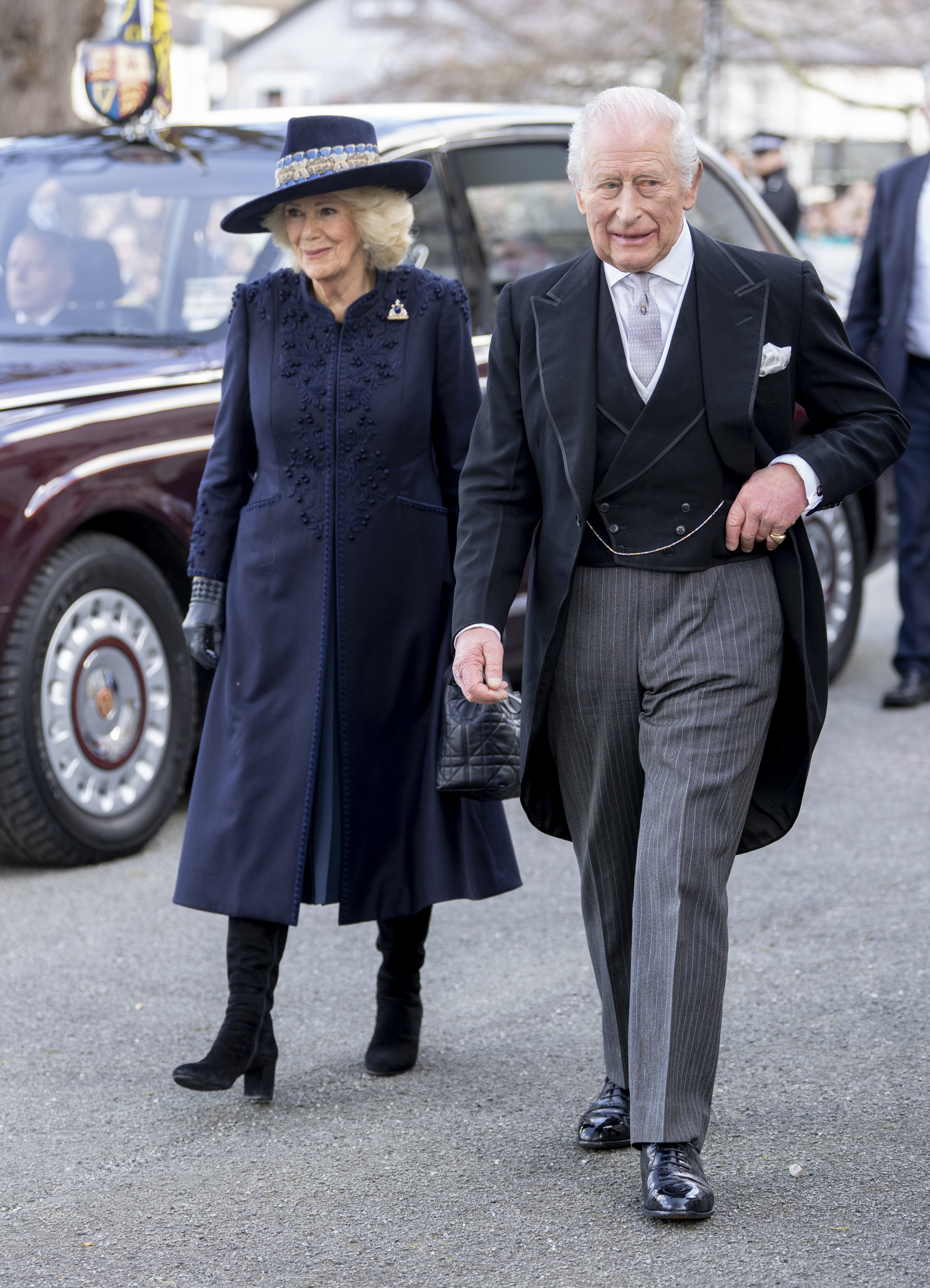 Queen Camilla wearing a blue coat walking next to King Charles in a suit