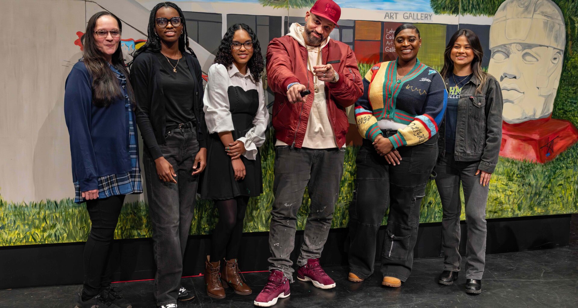 A group of art students, their professor, and The Kid Hero pose in front of a mural