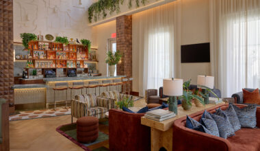 Modern hotel lounge designed by LEGEARD STUDIO, featuring a stylish bar, comfy sofas and armchairs, large windows with sheer curtains, and lush greenery decor on walls and shelves.