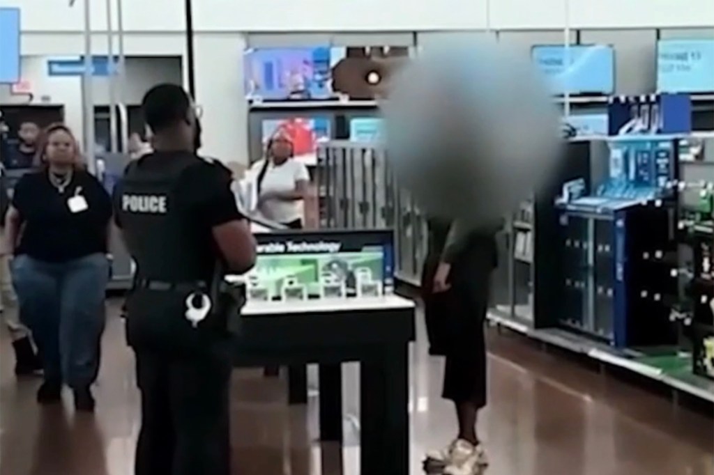 A police officer in a dark uniform stands with their back to the camera inside a store, with customers and merchandise visible around them.