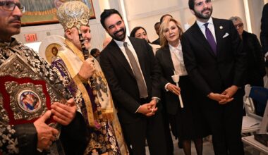 A Greek Orthodox Archbishop in ornate gold and purple vestments stands beside a smiling man in a dark suit inside a church.