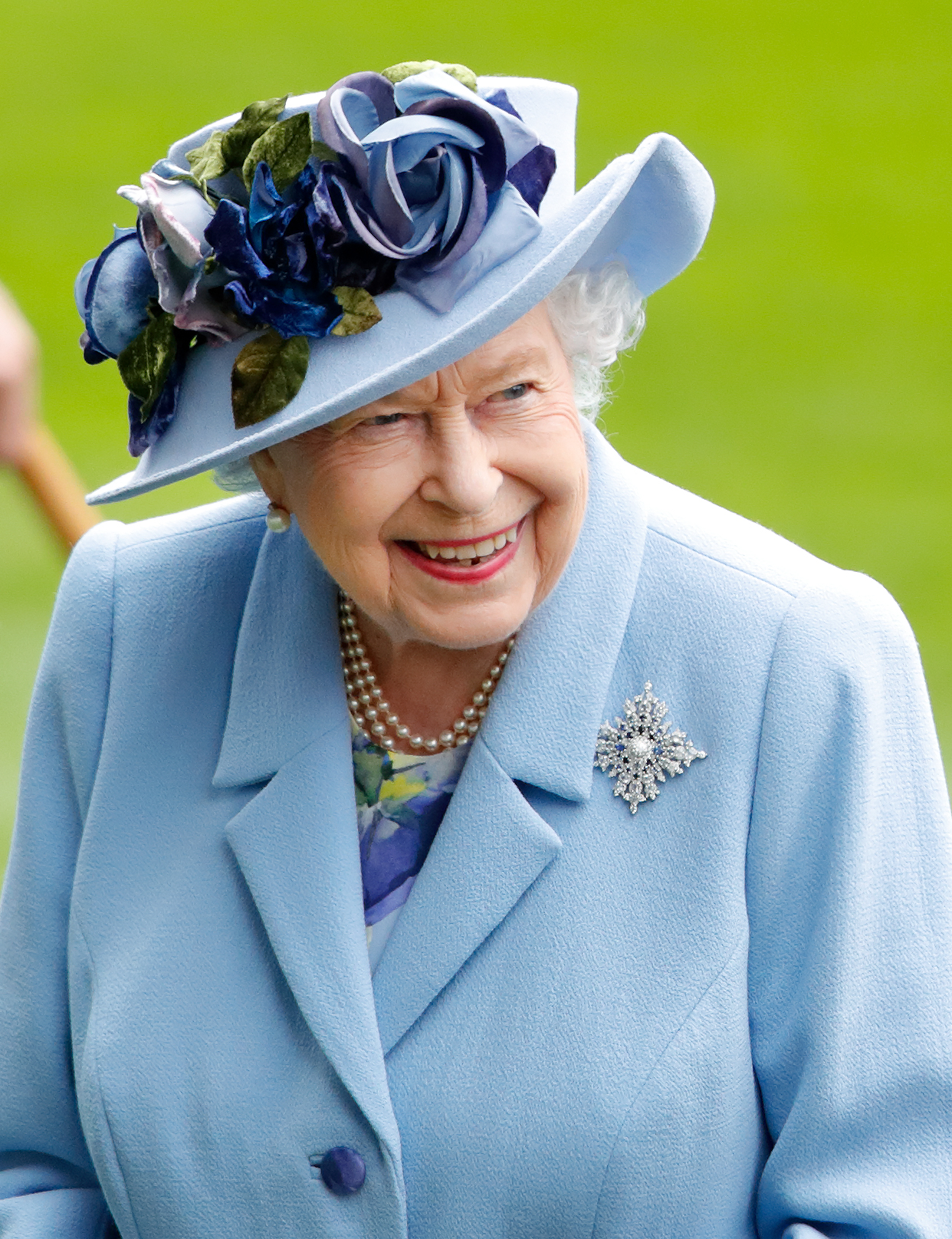 Queen Elizabeth wearing a blue hat with roses on it and a blue coat