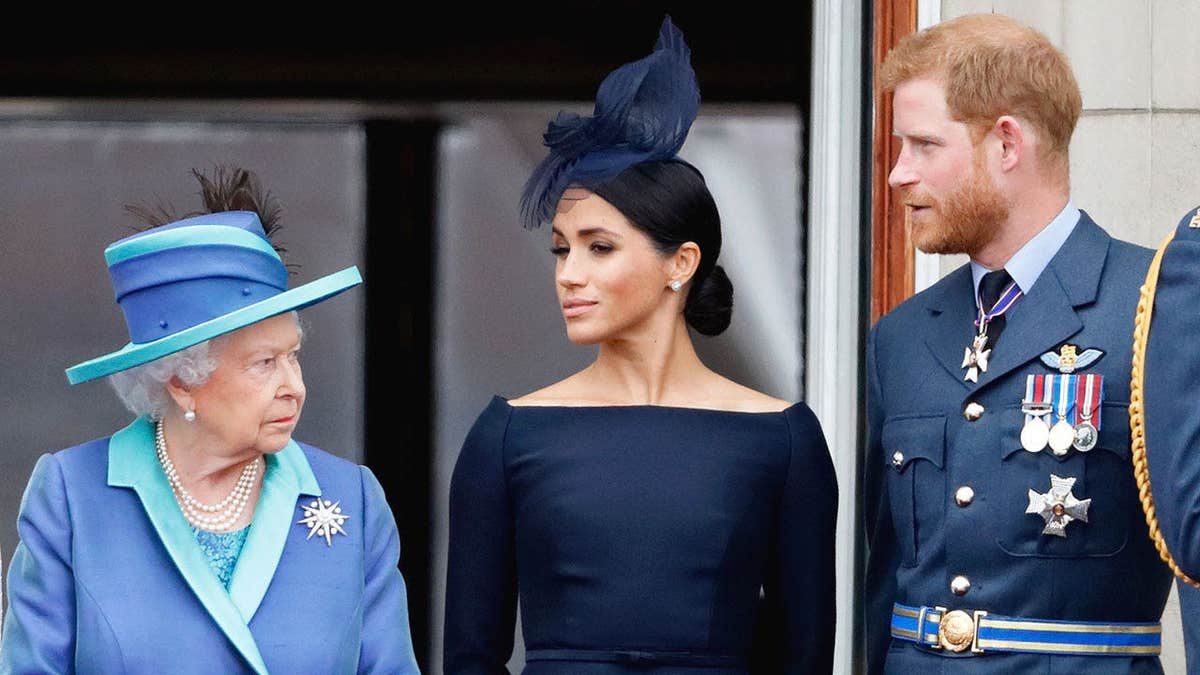 Queen Elizabeth, Meghan Markle and Prince Harry in formal wear standing on the balcony of Buckingham Palace.