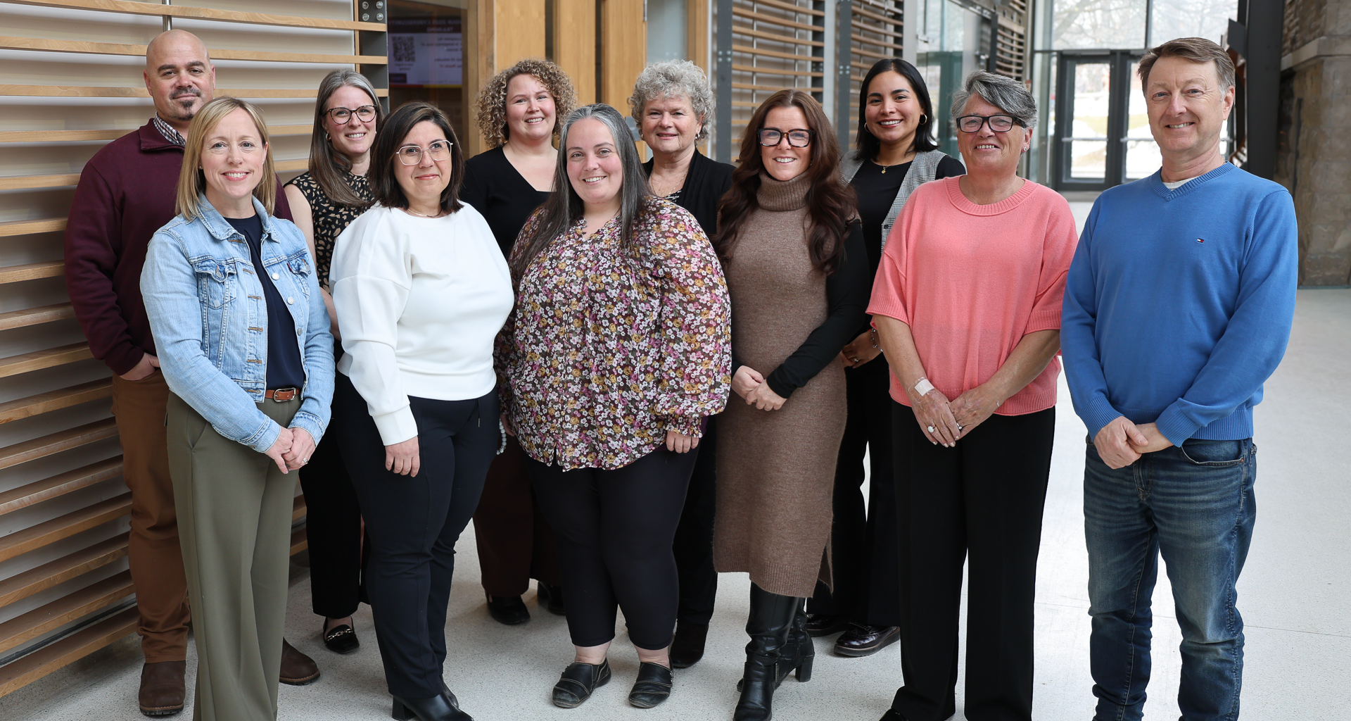 diverse group of Queen's staff members standing in a group and smiling at the camera