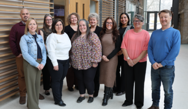 diverse group of Queen's staff members standing in a group and smiling at the camera