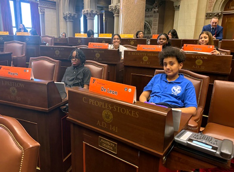 Students sit at desks in a formal setting.