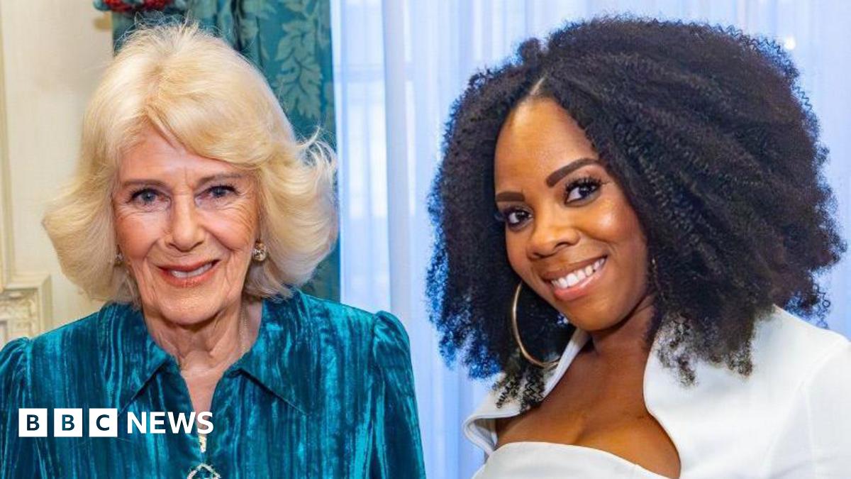 Selina Brown, on the right, has curly black hair to her shoulders and wears a white top while smiling. Queen Camilla, on the left, has shorter blonde hair and smiles, wearing a turquoise dress.