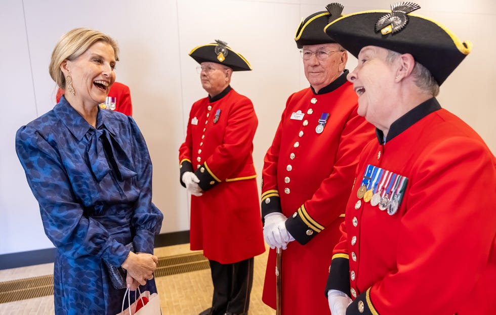 Interaction between a woman in a blue dress and men in ceremonial red uniforms.