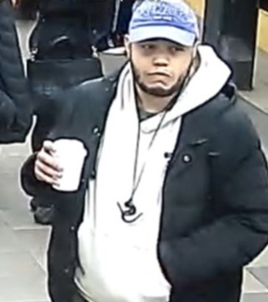Slightly blurred image of Gustavo DeJesus-Torres, a bank robbery suspect, wearing a blue cap, white hoodie, and black jacket, holding a white cup.