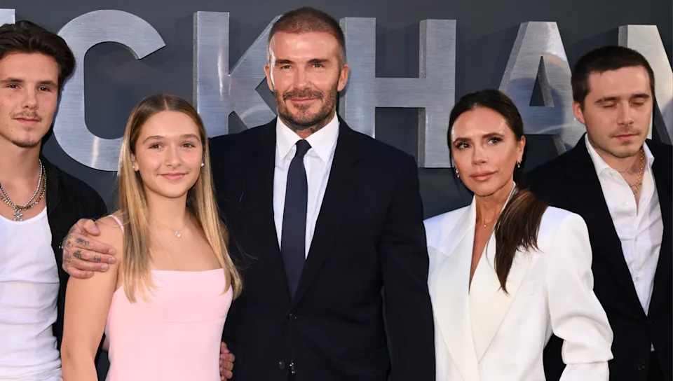 David and Victoria Beckham with their children at an event. David is in a suit, and Victoria wears a white outfit.