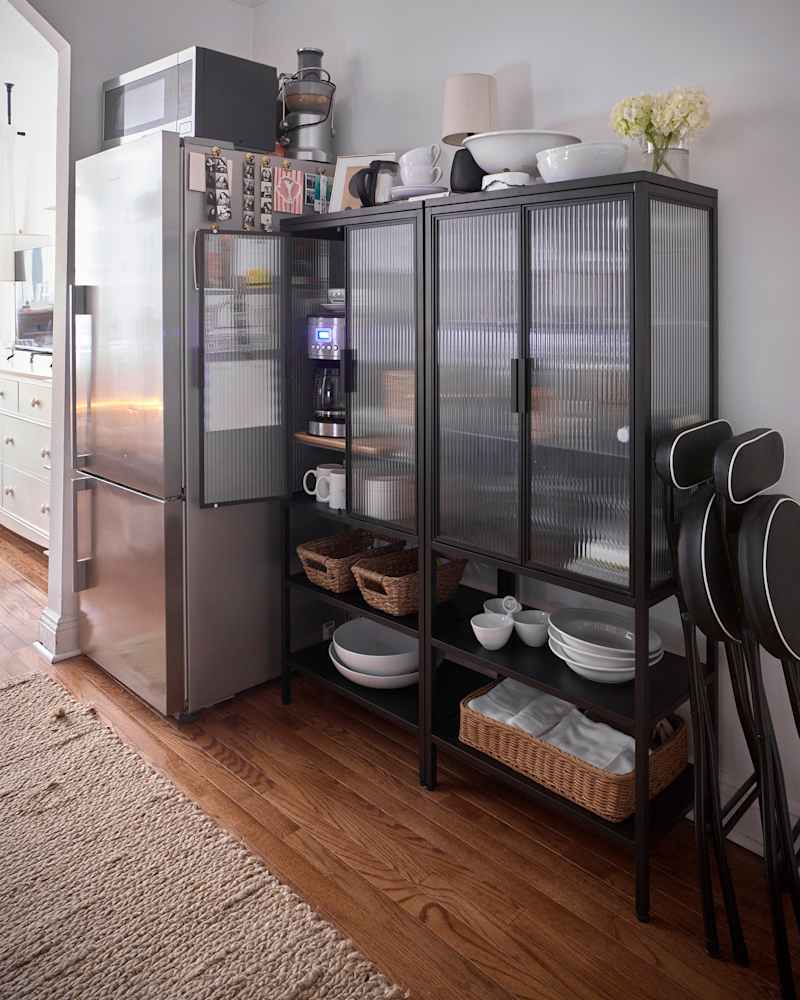 Modern kitchen corner featuring a stainless steel refrigerator, a black glass-front cabinet with dishes, coffee maker, and decorative items.