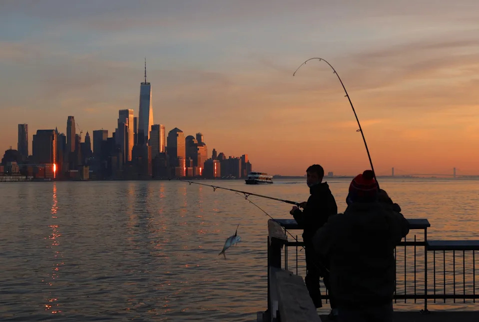 HOBOKEN, NJ - DECEMBER 11: A fisherman reels in a fish from the Hudson River as the sun sets on lower Manhattan and One World Trade Center in New York City on December 11, 2020 in Hoboken, New Jersey. (