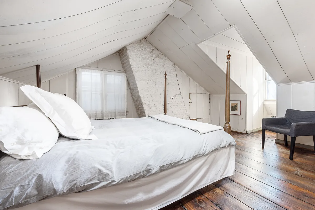 bedroom with white walls, slanted ceilings, wood floor