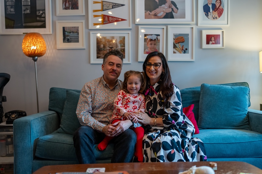 A couple sitting on the couch with their daughter.
