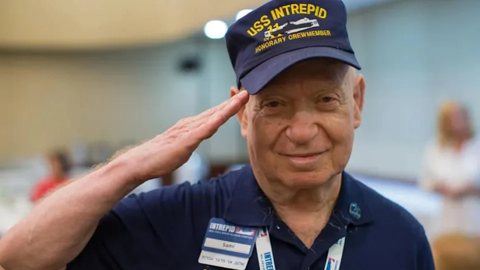 Holocaust survivor Sami Steigmann gives a salute while wearing his USS Intrepid volunteer uniform.