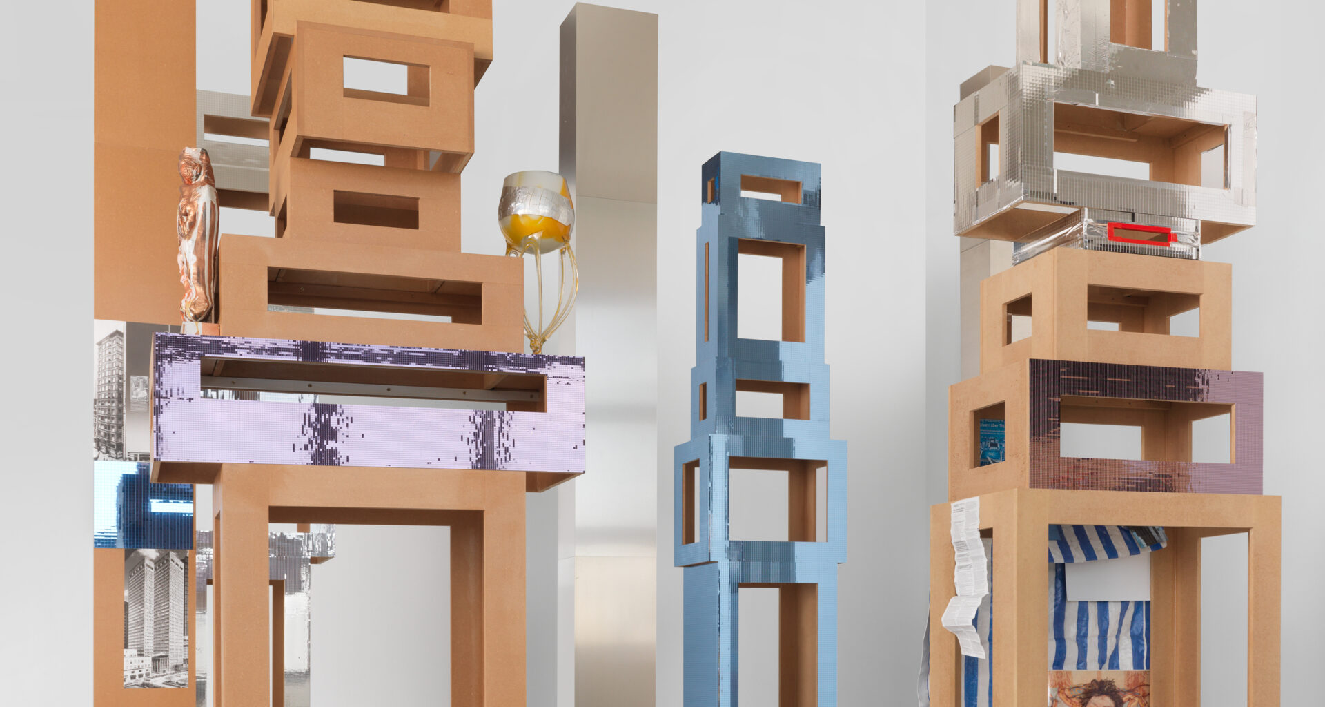 Isa Genzken, Untitled (4 Türme, 3 Stelen), 2015. Installation of 7 parts (4 towers, 3 columns), MDF, plastic, mirror foil, glass, cigarette, tin foil, spray paint, plaster, acrylic, adhesive tape, photographs, metal, aluminium, paper; dimensions variable, approx. 132 ⅘ × 141 ¾ × 118 inches. Courtesy the artist and Galerie Buchholz.