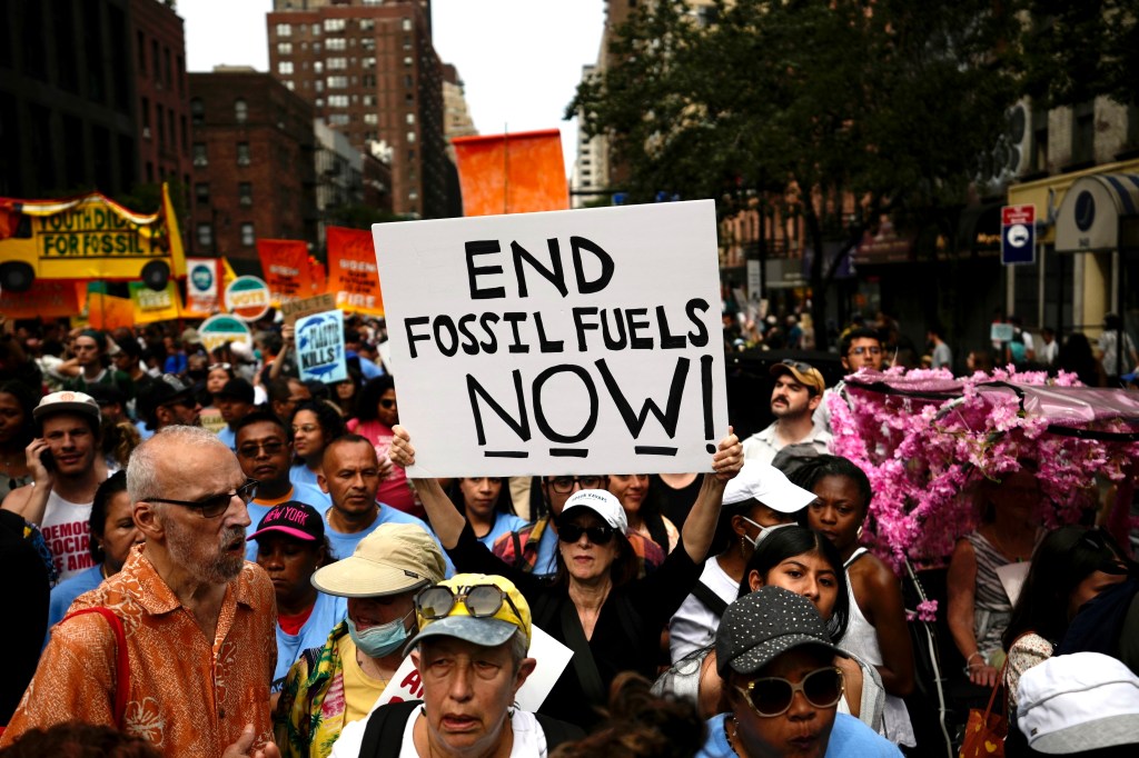 A person holds a sign reading "END FOSSIL FUELS NOW!" at a climate protest.