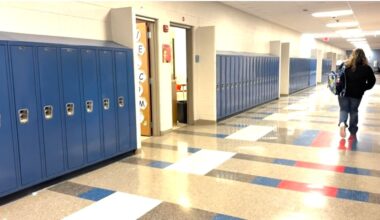 student walks away from camera down school hallway, carrying a backpack over their left shoulder