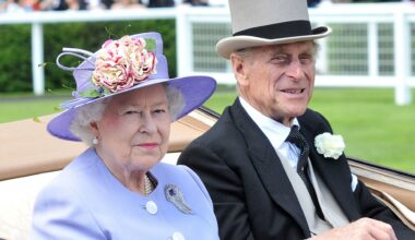 Queen Elizabeth wearing a lilac hat and coat and sitting next to Prince Philip who wears a top hat