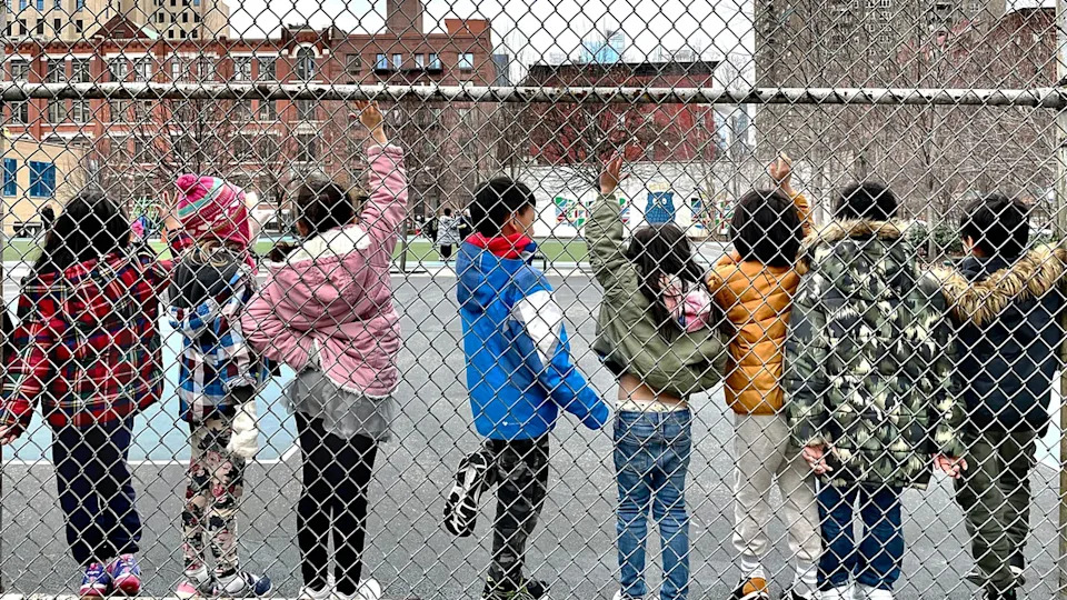 Students line up along a chain link fence.
