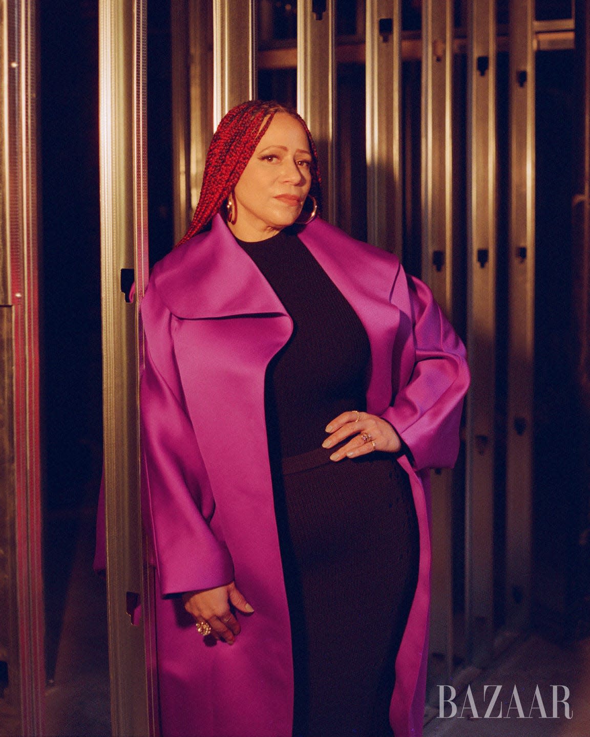 Portrait of a person wearing a striking purple coat and black dress, posed against a metallic background.