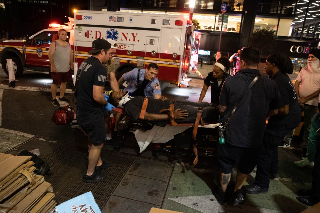 Police and first responders at the scene of an E-bike versus taxi accident, with a crashed taxi and another vehicle in the background.