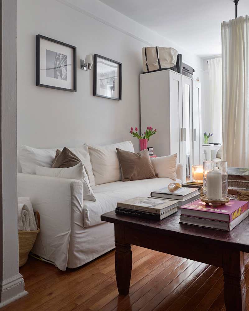 Cozy living room with a white sofa, decorative pillows, a wooden coffee table stacked with books, and a vase of tulips.