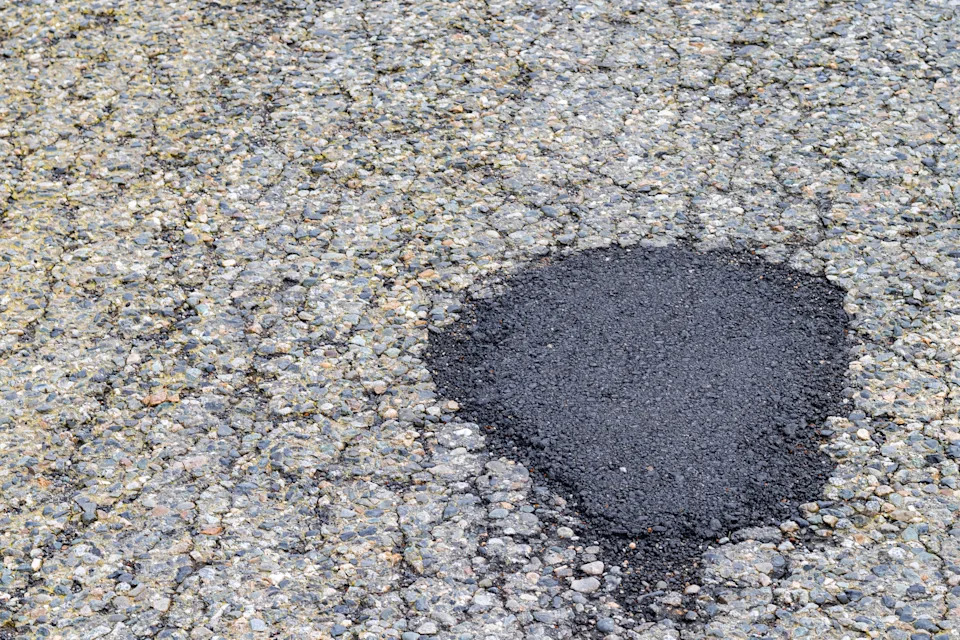 Repaired pothole on a cracked asphalt road, visibly patched with new material