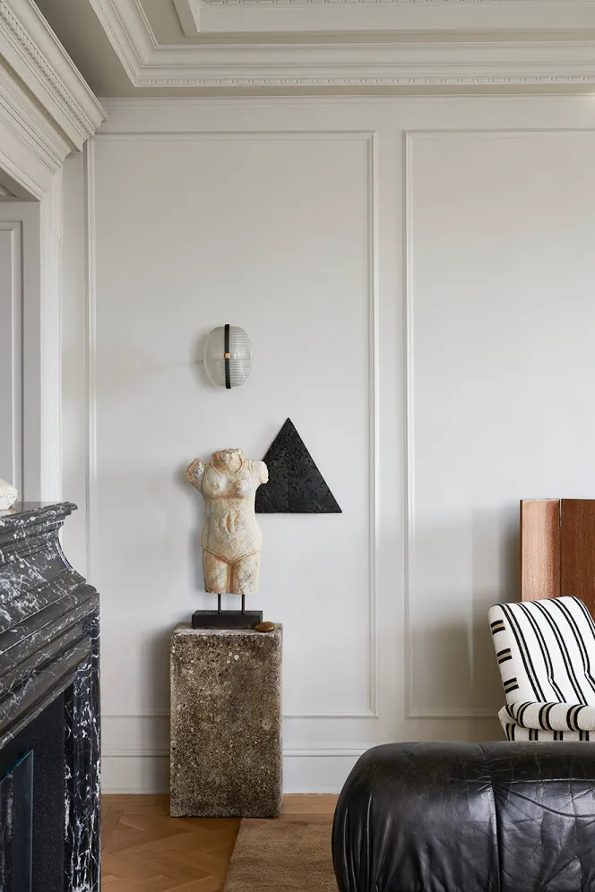 An off-white interior with a marble torso statue on a concrete pedestal.