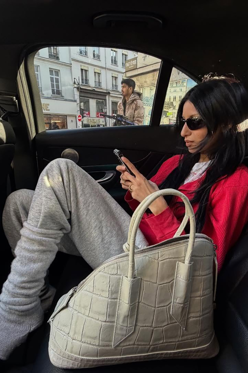 a woman wearing a red top, gray sweatpants, and a cream croc-embossed handbag