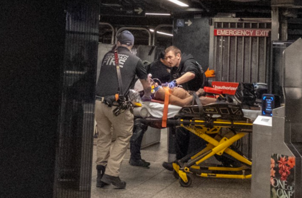Emergency medical personnel attending to a patient on a stretcher in what appears to be a subway station.
