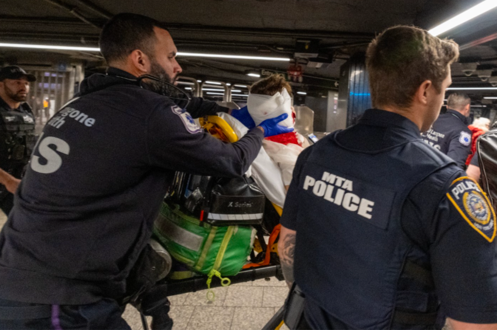 Emergency services and MTA police attend to a victim on a stretcher in a subway station.