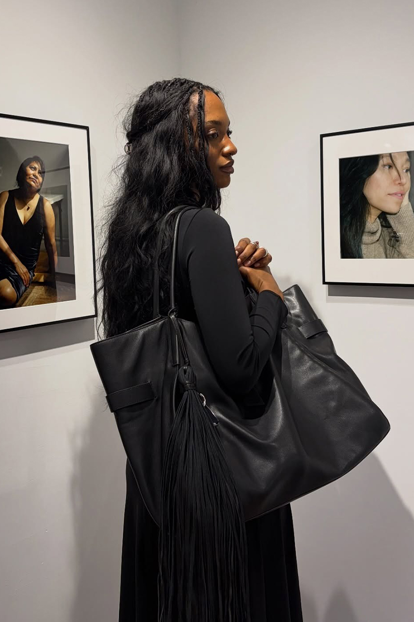 a woman wearing a black long-sleeve shirt, and a black leather bag