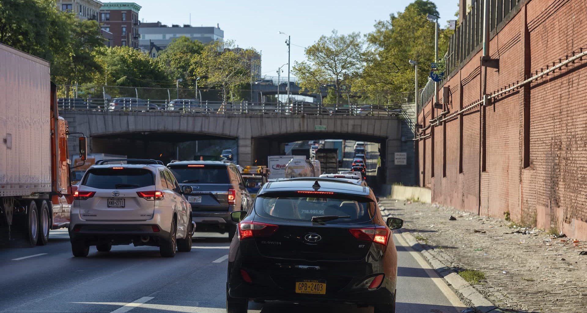 A view of a busy highway with cars, overhead bridge, and buildings surrounded by greenery.