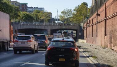 A view of a busy highway with cars, overhead bridge, and buildings surrounded by greenery.
