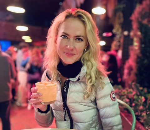 Writer Sadie Whitelocks smiles with a cocktail in a puffer jacket in Koreatown, New York