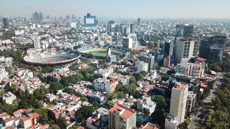 An aerial view of Mexico City, showing skyscrapers, stadiums, and parks