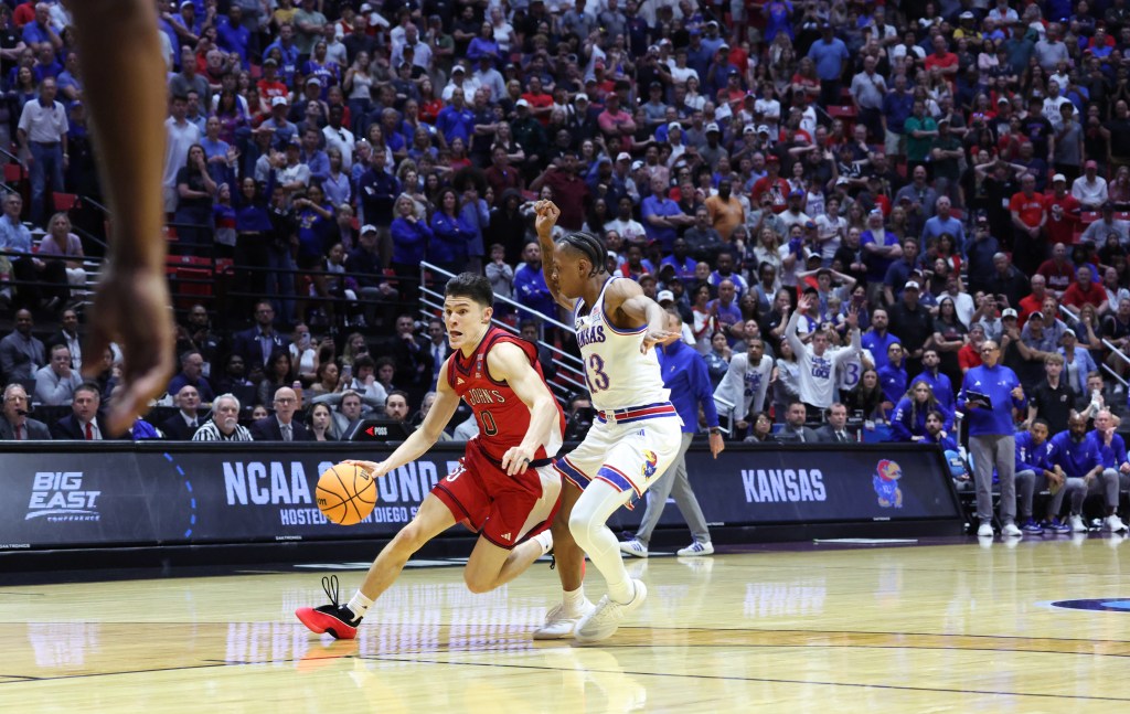 St. John's Red Storm guard Dylan Darling dribbling the ball against a Kansas Jayhawks player.