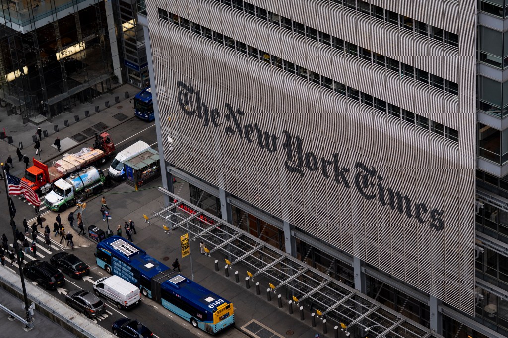 The New York Times Building facade with its name prominently displayed, looking down at people and vehicles on the street below.