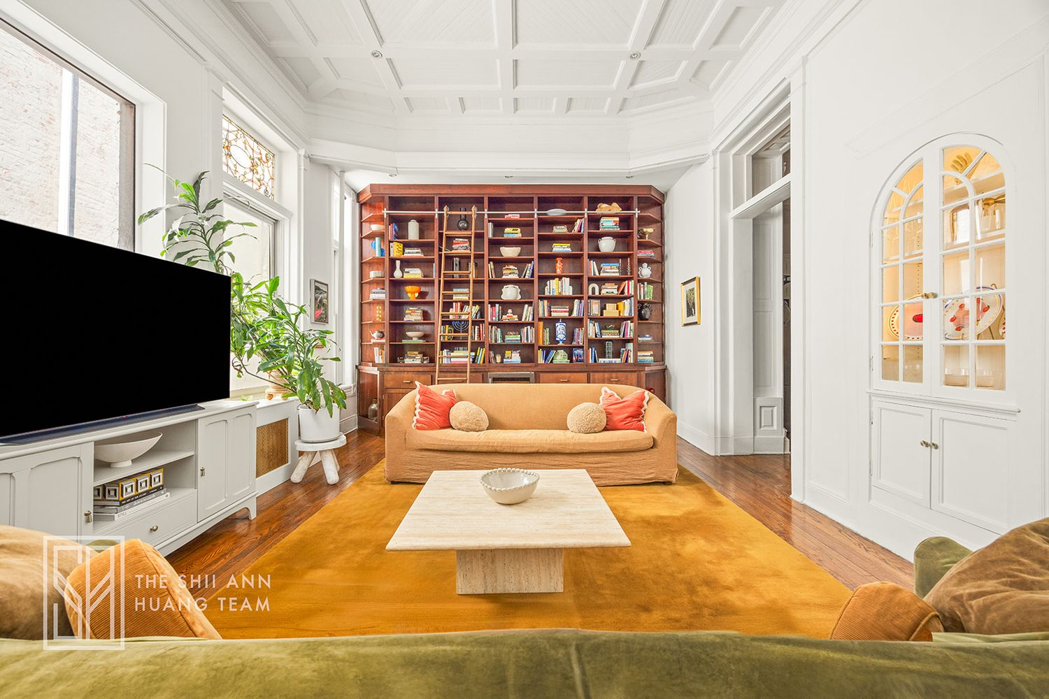 living room with coffered ceiling, wall ofbookshevles, built-in niche