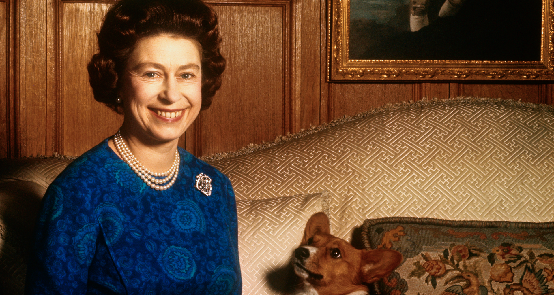 Queen Elizabeth sitting on a sofa with a corgi