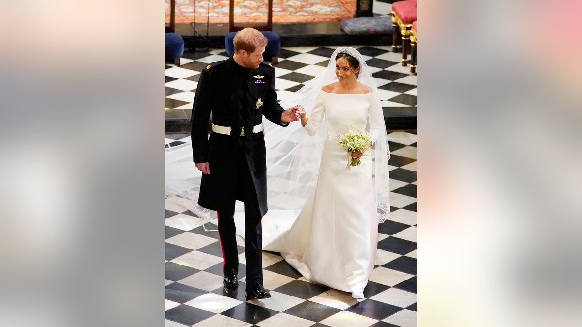 Prince Harry in a black suit holding Meghan Markle's hand at Windsor Castle